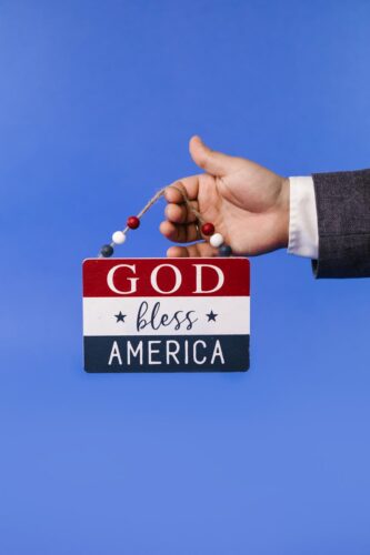 A hand holding a 'God Bless America' sign against a blue backdrop, symbolizing patriotism.