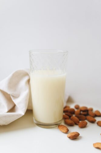 Close-up of a glass of almond milk surrounded by almonds on a white surface, emphasizing vegan and plant-based lifestyle.