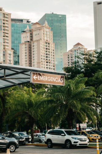 Vertical shot of cityscape featuring high-rise buildings, parked cars, and an emergency sign.