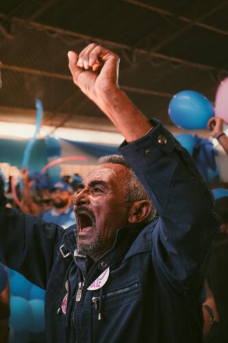 Senior man passionately cheering at a colorful festival in Brazil, surrounded by balloons.