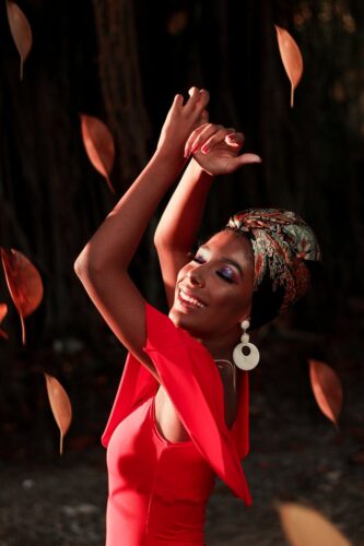 Joyful woman dancing outdoors, surrounded by falling leaves at sunset.