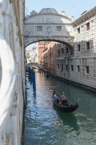 Gondola glides through Venice's canal under the historic Bridge of Sighs, capturing Venetian charm.