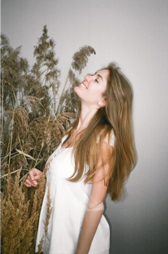 Happy woman in white dress enjoying nature indoors with dried plants.