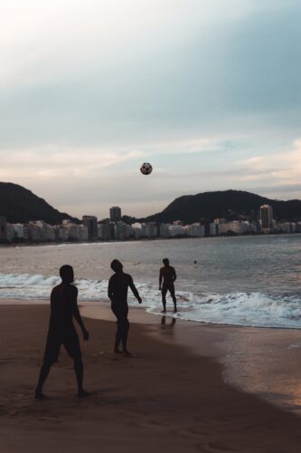 People playing volleyball on a beach with city skyline and hills in the background at dusk.