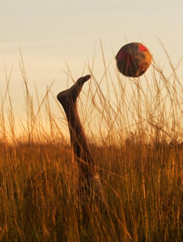 A young boy plays soccer in tall grass at sunset in Rio de Janeiro, embracing freedom and joy.
