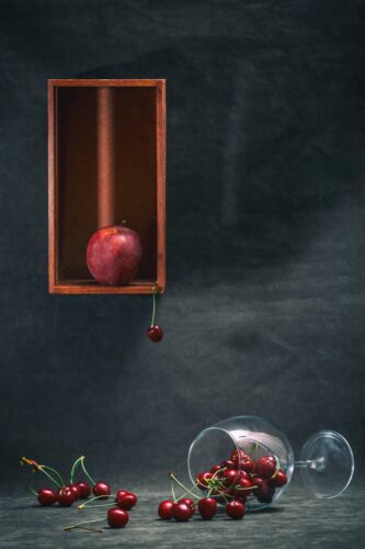 Artistic still life of apples and cherries with a glass, highlighting a contrast of colors and textures.