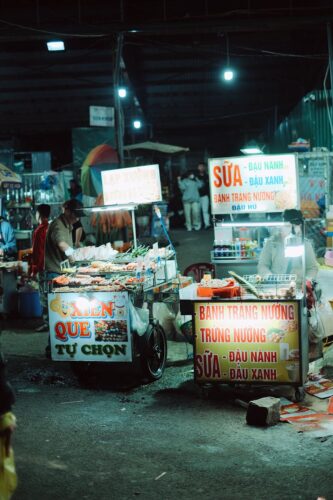 Bustling night market with food stalls illuminated by colorful lights, showcasing Vietnamese street cuisine.