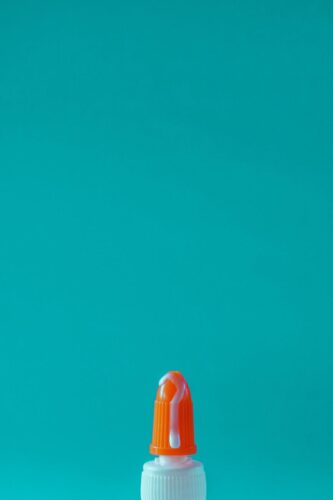 Vivid image of glue bottle with orange cap against teal backdrop.