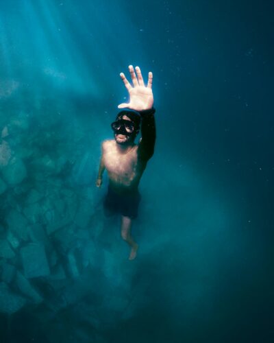 Man diving underwater with sunlight streaming through, captured in São Thomé das Letras.