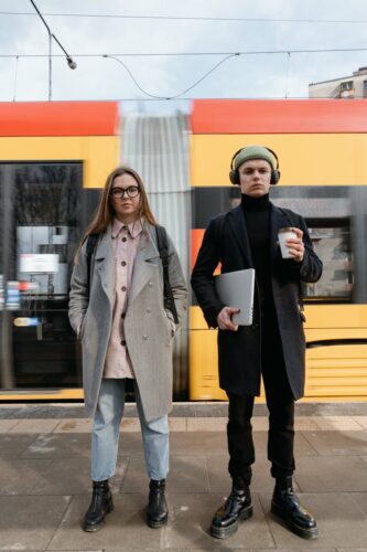 Two young adults standing at a bustling train station with a moving train in the background.