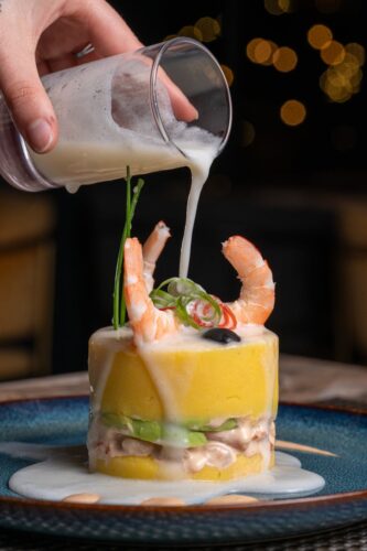 Delicious Peruvian causa with shrimp, avocado, and sauce for a gourmet experience.