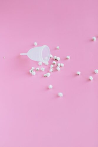 White menstrual cup with flowers on a pink background symbolizing femininity and hygiene.
