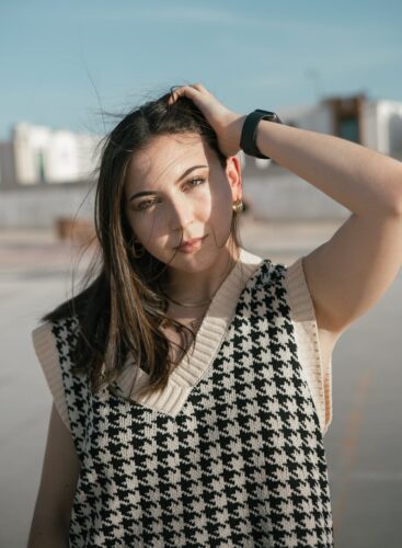 Portrait of a young woman in a stylish houndstooth sweater, enjoying a sunny day outdoors.
