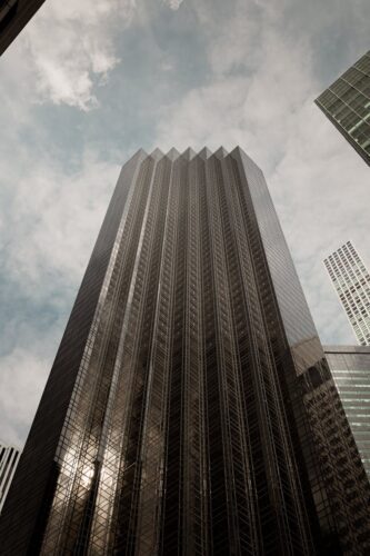 A striking view of a modern skyscraper in New York City, captured from below with a cloudy sky backdrop.