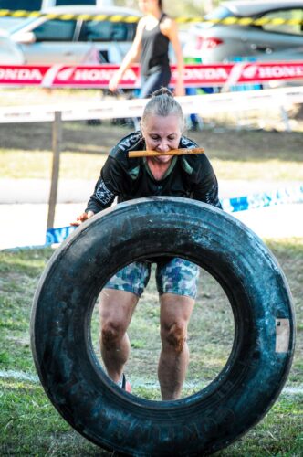 Woman participating in a tire flipping challenge outdoors, showcasing strength and determination.