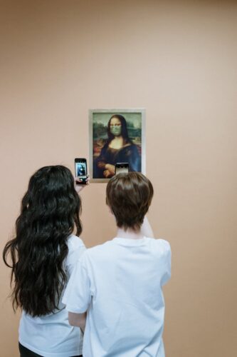 Two people capturing the Mona Lisa with face mask on their smartphones in a gallery.