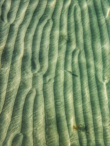 A mesmerizing view of sandy ripples underwater near Arraial do Cabo, Brazil, with sunlit patterns.