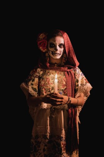An adult in traditional Day of the Dead attire holds a candle in Mérida, Mexico.