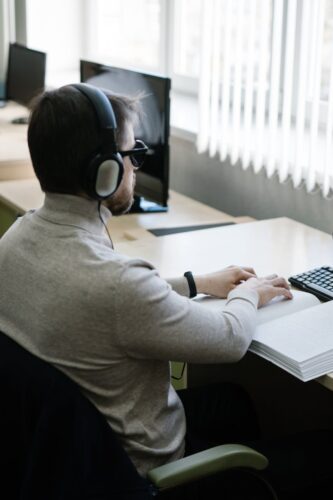 A visually impaired man reading a braille book indoors with headphones on.